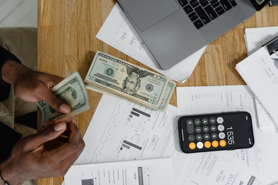 Close-up of hands counting cash on desk with calculator, charts, and laptop, illustrating financial management.